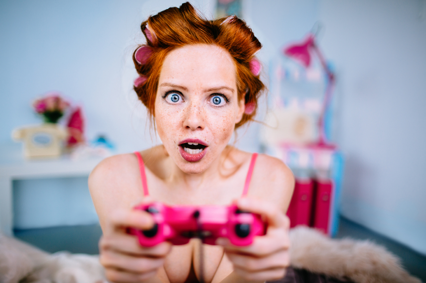 Close up of young woman playing video games in bed with curlers in her hair