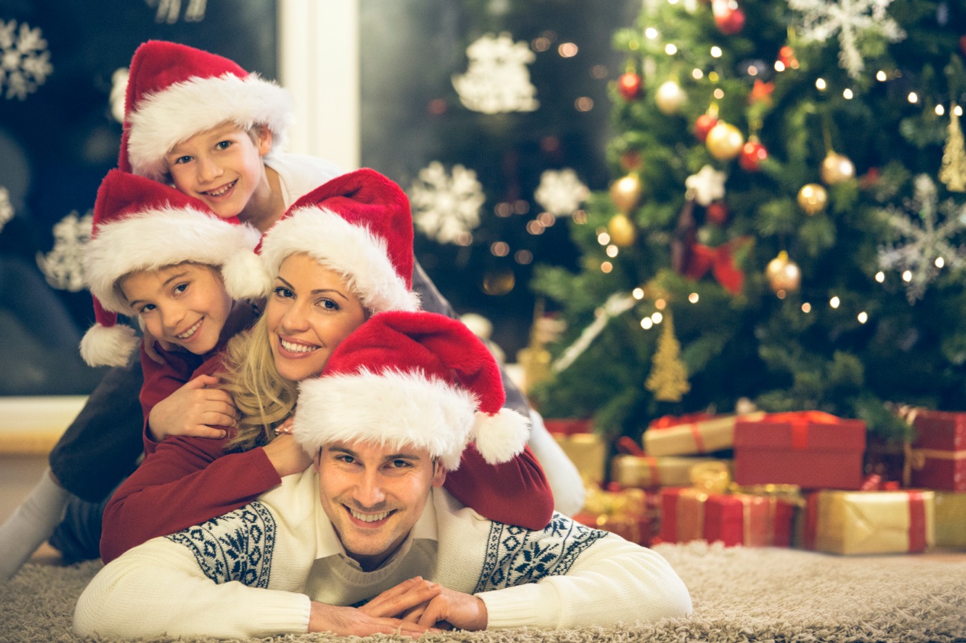 Happy family with two children with Santa hats lying down on the floor, looking at camera.