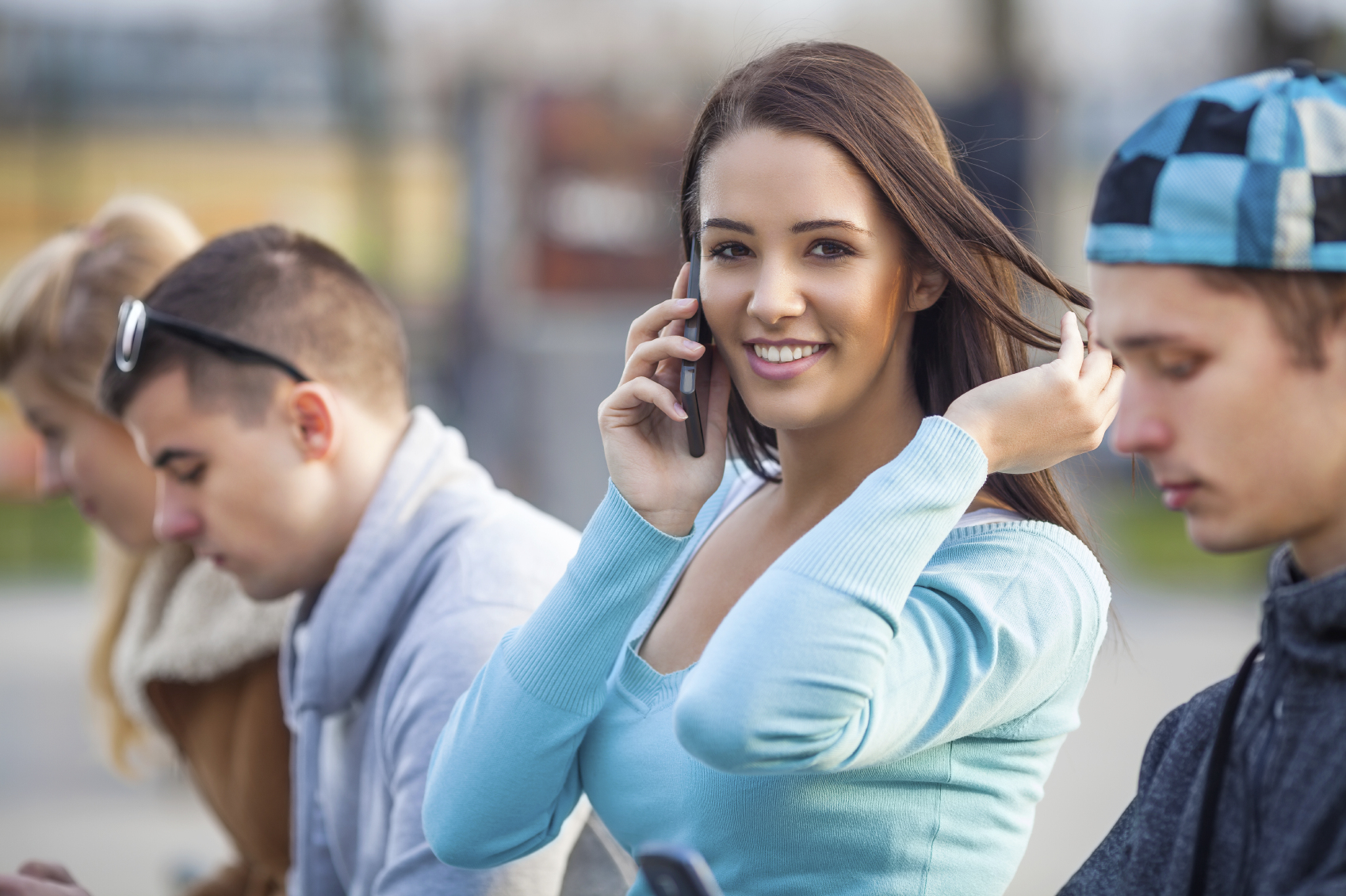 Portrait of beautiful young woman talking on the phone with her friends in the background using their mobile phones